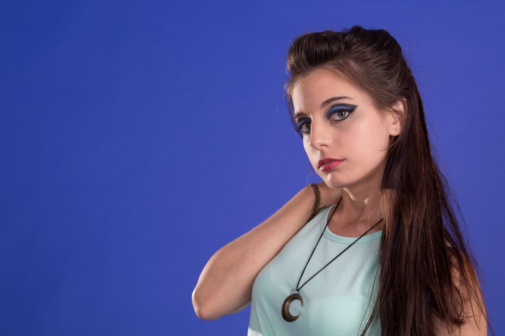Fotografía de retrato de estudio en fondo azul, modelo femenina. Esquema de 3 luces con recorte y clave media.
