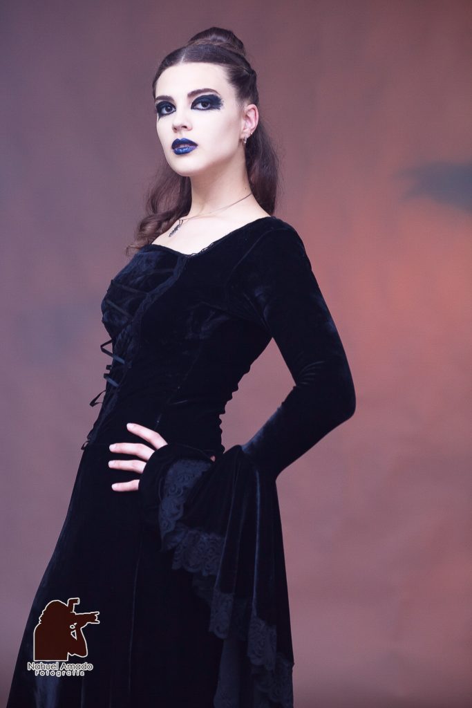 Foto editorial con vestidos de altwa costura, maquillaje artístico de liz-trent. Outfit gótico, iluminación de estudio, luces rojizas en fondo con sobra de cuervo proyectada.  