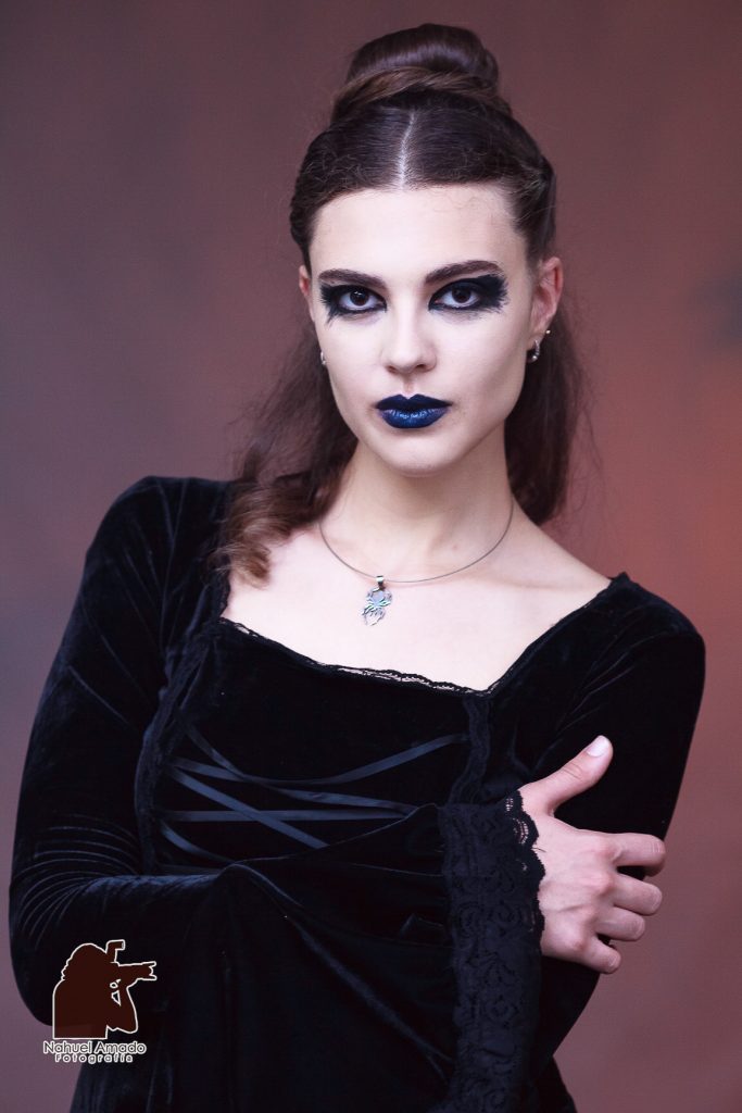 Foto editorial con vestidos de altwa costura, maquillaje artístico de liz-trent. Outfit gótico, iluminación de estudio, luces rojizas en fondo con sobra de cuervo proyectada.  